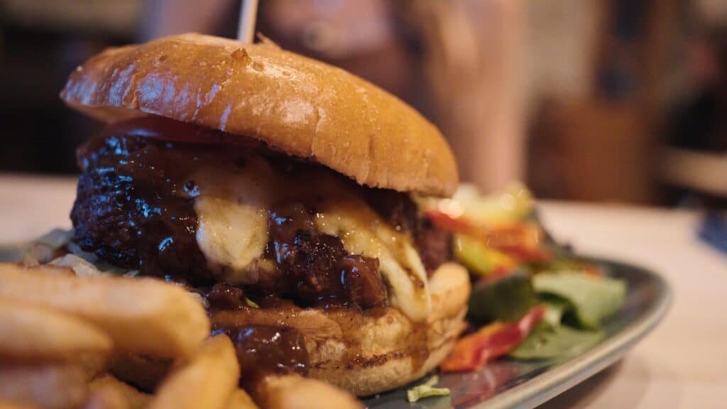 Thick burger topped with melted cheese and caramelized onions inside a soft bun served with chips and salad. The hearty burger represents modern pub dishes often served alongside traditional Scottish food.