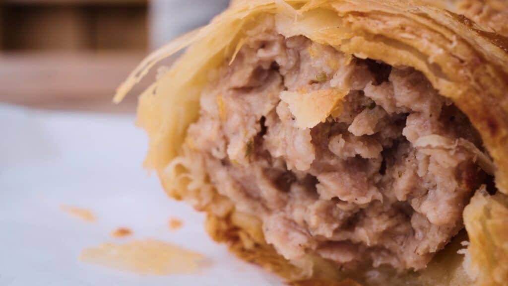 Close up of a flaky golden pastry broken open to reveal a savory minced meat filling inside. This traditional English food pastry shows its rich texture and hearty interior.