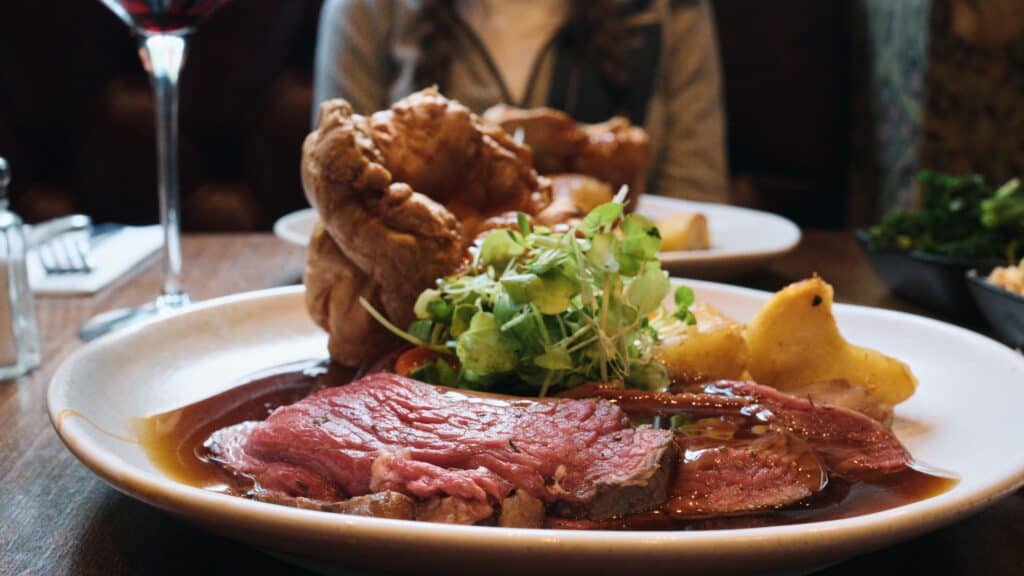 Plate of roast beef covered in gravy with Yorkshire pudding and vegetables served at a dining table. This traditional English food meal is presented as a classic Sunday roast.