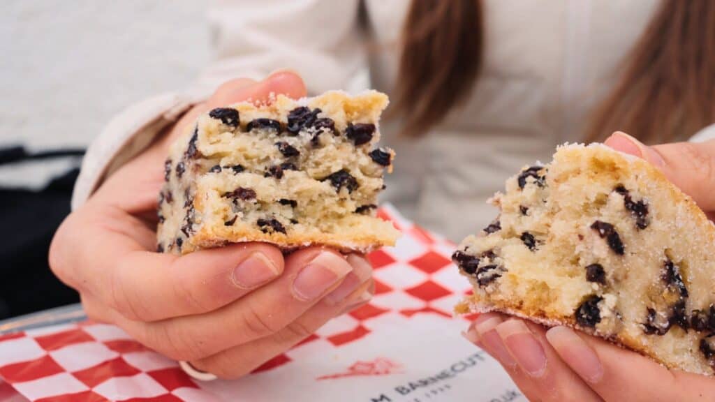 Hands hold and pull apart a crumbly currant filled cake showing a soft fluffy interior with dried fruit throughout. This traditional English food bake highlights a simple sweet treat often enjoyed with tea.