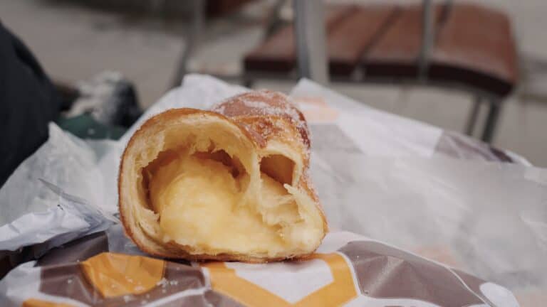 Custard filled pastry cut open on a paper wrapper with thick cream filling spilling out from the center. The golden flaky pastry highlights one of the best food stops in Barcelona for sweet pastries and local desserts.