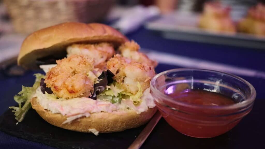 Fried shrimp sandwich with lettuce and creamy filling served beside a small bowl of dipping sauce. Casual seafood sandwiches like this are an example of where Madrid is expensive compared to other cities in Spain.