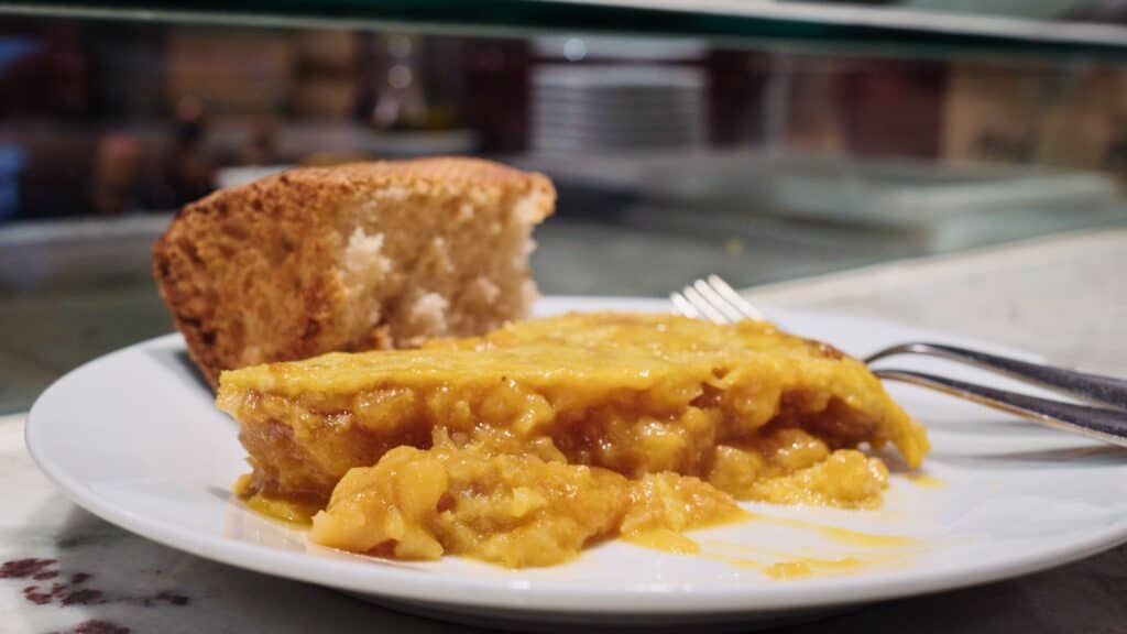 Slice of Tortilla Espanola served on a white plate at a restaurant counter in Bilbao. The creamy filling and close up presentation highlight one of the best restaurants in Bilbao for traditional comfort food.