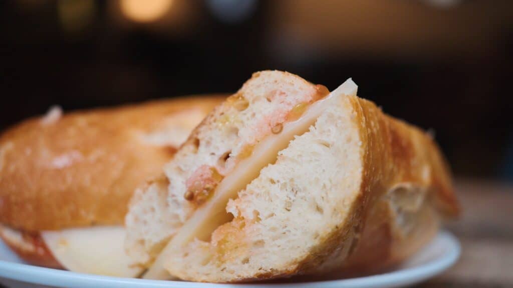 Baguette sandwich cut in half with melted cheese and salmon filling visible between soft bread layers. Fresh seafood sandwiches like this are part of the best food in Barcelona for quick lunches and cafe meals.