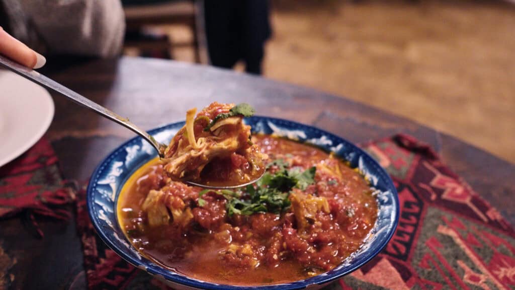 Spoon lifting a bite of rich tomato based chicken stew with herbs from a bowl, highlighting a hearty dish from traditional Georgian foods.