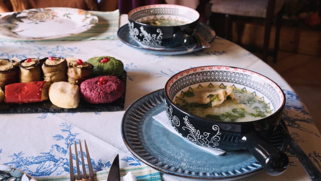 Table setting with patterned bowls of soup and a platter of vegetable appetizers including eggplant rolls and colorful spreads, representing a variety of traditional Georgian foods.