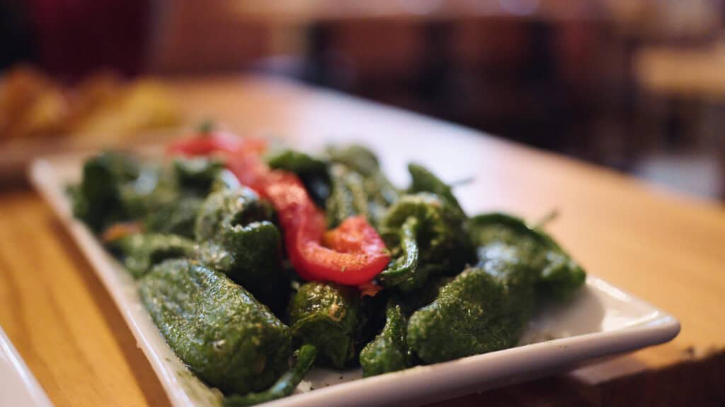 a plate of small green peppers topped with flaky sea salt