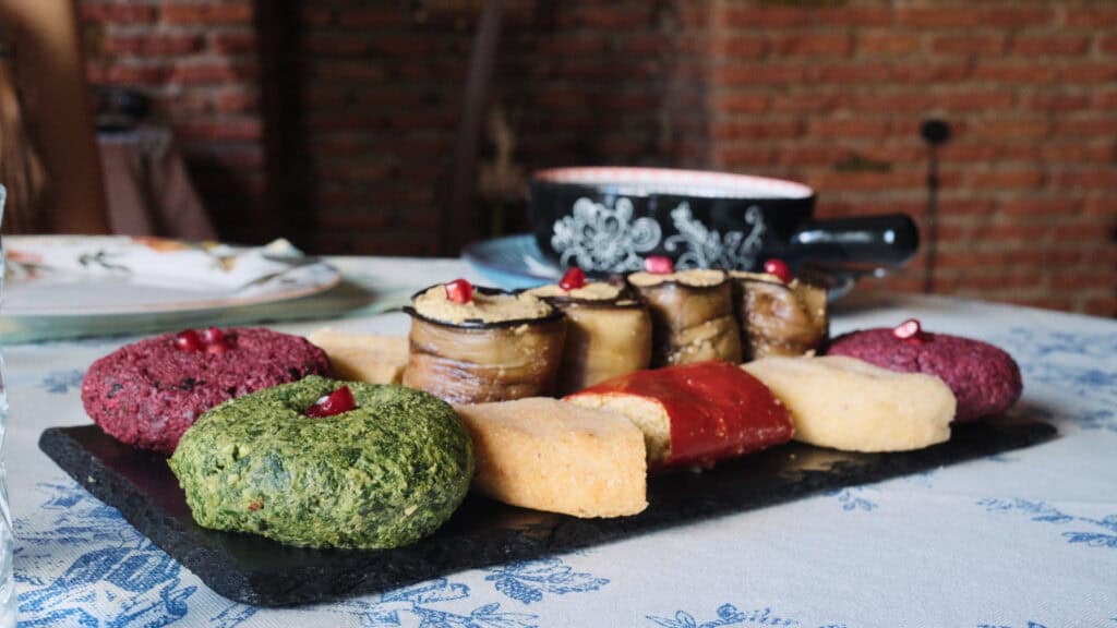Colorful platter of vegetable patties, roasted eggplant rolls, and bread garnished with pomegranate seeds, highlighting traditional Georgian foods and their rich textures.