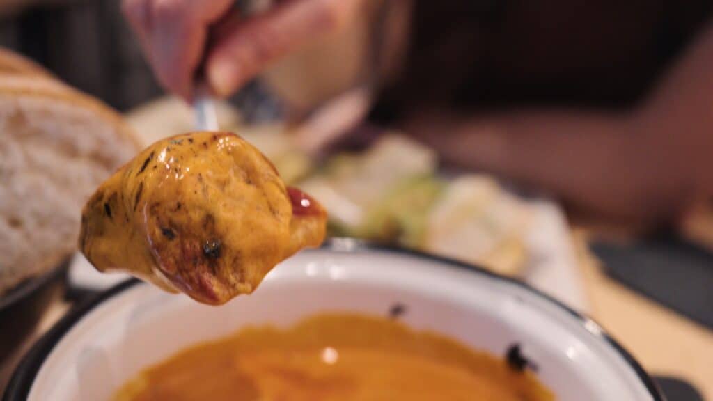 A fork holds a sauce covered bite of food above a bowl, with a person leaning in to take a bite in the background. The close up emphasizes the rich flavors typical of dishes at restaurants in calle ibiza madrid.