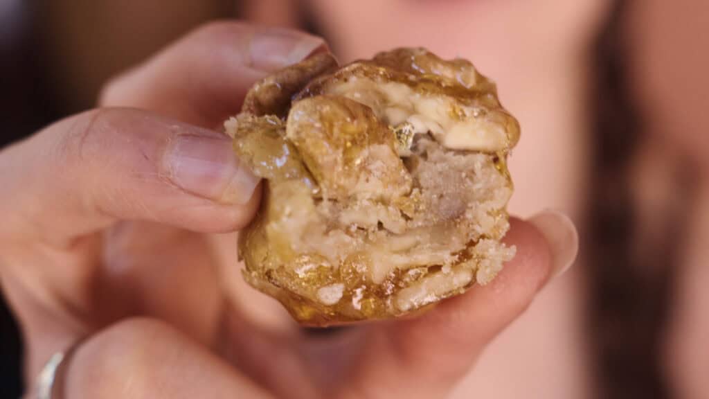 Close up of a walnut filled pastry piece held between fingers with visible layers and syrup glaze, a sweet example of traditional Georgian foods.