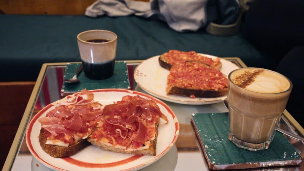 Toast topped with tomato spread and cured ham served beside coffee drinks on a cafe table in Madrid. Affordable cafe breakfasts like this show that Madrid is not expensive for simple local meals.