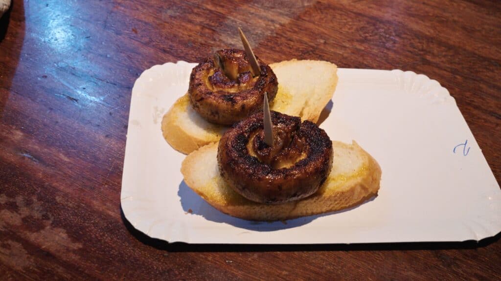 Two grilled mushrooms stuffed with savory filling and served on slices of bread with toothpicks holding them together. The charred edges and simple presentation reflect classic pintxos at the best restaurants in Bilbao.