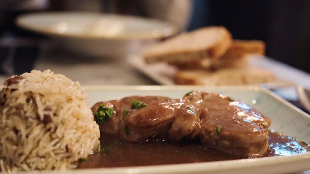 Tender meat medallions covered in brown gravy served beside a mound of rice on a rectangular plate. Traditional comfort dishes like this showcase where to eat in Barcelona for hearty local meals.