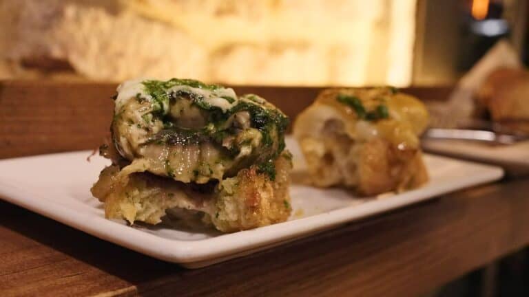 Cheesy stuffed mushroom with herbs and melted cheese resting on toasted bread on a small white plate. The rich seafood pintxo highlights the creative dishes served in the best restaurants in Bilbao.