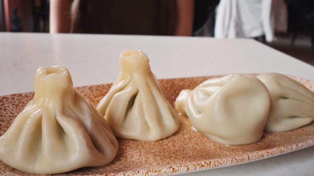 Three steamed dumplings with pleated tops served on a plate, a staple of traditional Georgian foods known for their soft dough and savory filling.