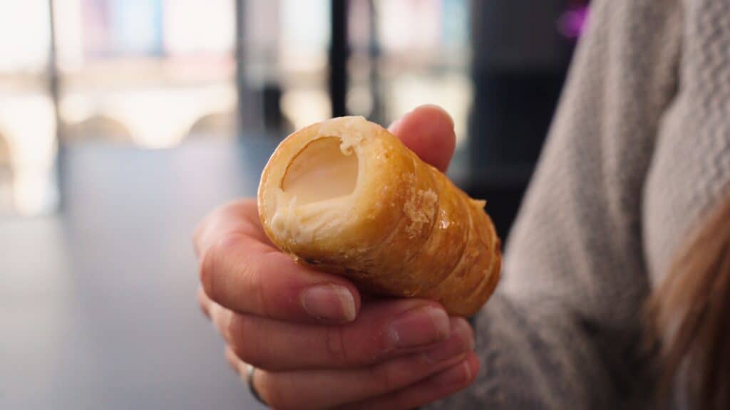 Hand holding a cream filled pastry roll with flaky golden layers and smooth white filling visible inside. The close up texture and fresh pastry showcase sweet treats from the best restaurants in Bilbao.