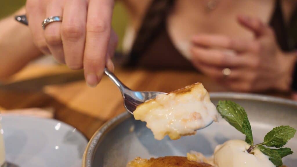 A spoon lifts a creamy dessert topped with caramelized glaze and a sprig of mint from a shallow bowl. The indulgent finish reflects the variety of sweets offered at restaurants in calle ibiza madrid.
