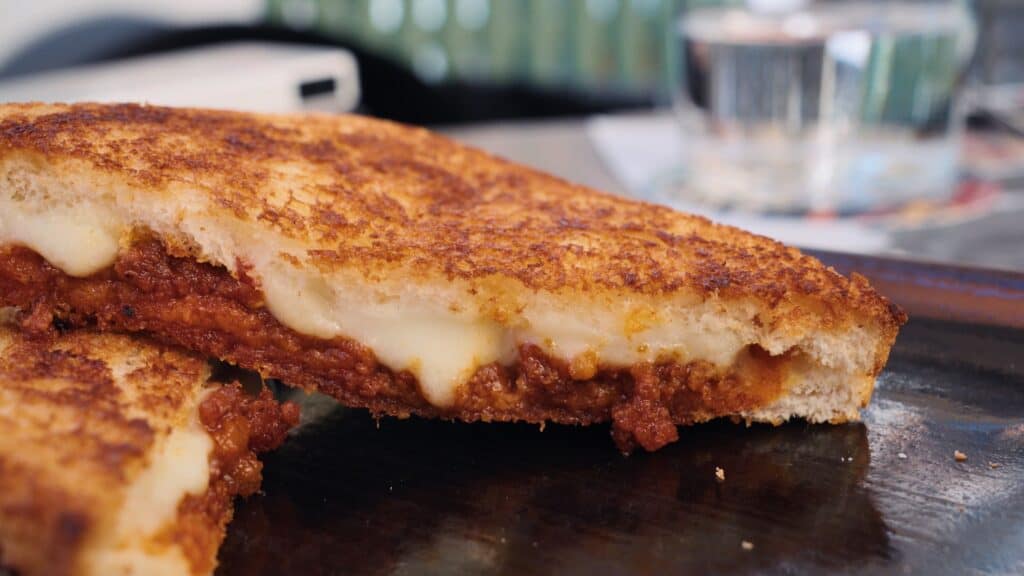 Crispy grilled sandwich sliced open to show melted cheese and rich tomato meat filling inside toasted bread. Gooey toasted sandwiches are part of the best food in Barcelona cafe scene.