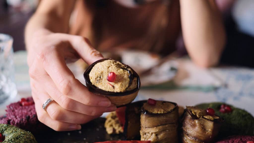 Hand picking up a rolled eggplant slice filled with walnut paste and topped with a pomegranate seed, a classic appetizer in traditional Georgian foods.