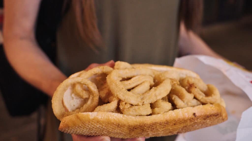 A hand holding a large sandwich filled with fried calamari rings