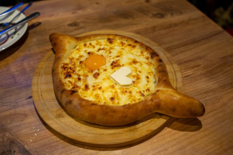 Boat shaped bread filled with melted cheese topped with a raw egg yolk and a pat of butter on a wooden board, a signature dish in traditional Georgian foods.