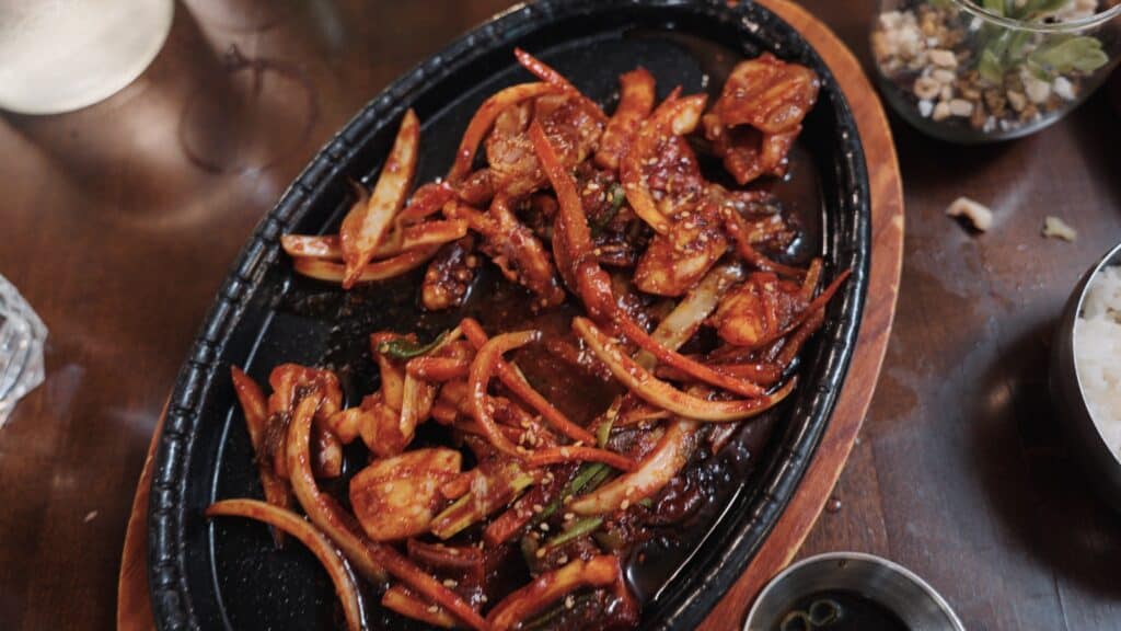 Sizzling platter filled with spicy stir-fried meat, onions, carrots, and vegetables coated in a glossy red sauce and sprinkled with sesame seeds. International flavors add variety to the best restaurants in Fort Dodge Iowa.