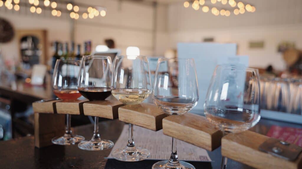 Wine flight featuring red, rosé, white, and sparkling wines served in stemmed glasses on wooden holders inside a bright tasting room. Local wineries and tasting experiences complement the best restaurants in Fort Dodge Iowa.